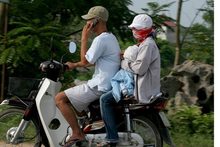 Không mũ bảo hiểm, chở theo trẻ em vẫn thản nhiên sử dụng điện thoại trên Đại Lộ Thăng Long.