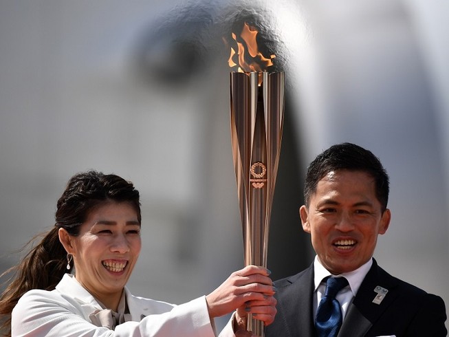 Hai VĐV Nhật Bản Tadahiro Nomura (phải) và Saori Yoshida (trái) gương cao ngọn đuốc Olympic Tokyo 2020. Ảnh: AFP.